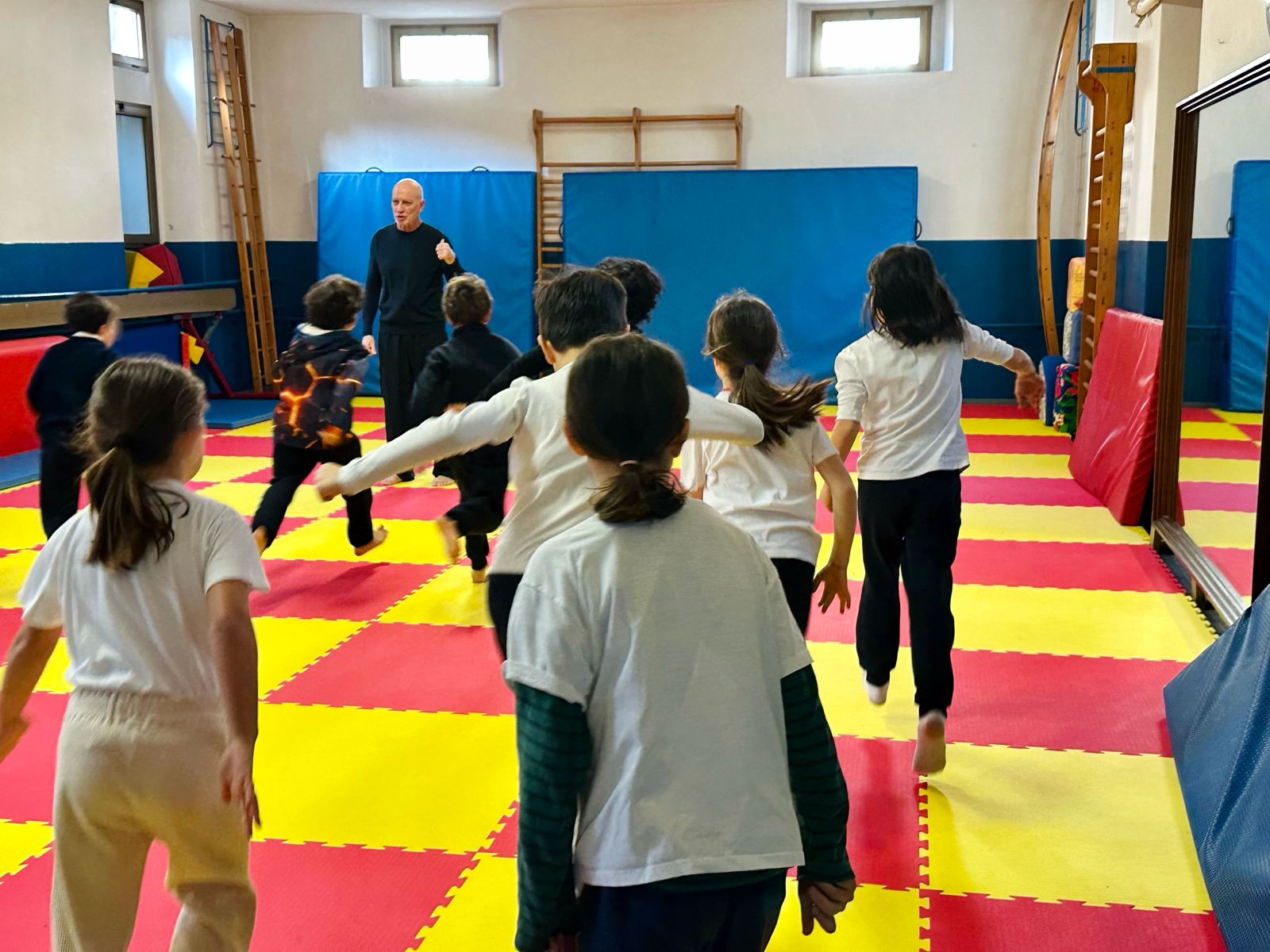 Bambini in movimento durante una lezione di psicomotricità sui tappeti gialli e rossi
